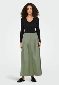 Maglietta nera a maniche lunghe con scollatura a V, abbinata a una gonna maxi plissettata verde chiaro con chiusura a bottone e tasche laterali.