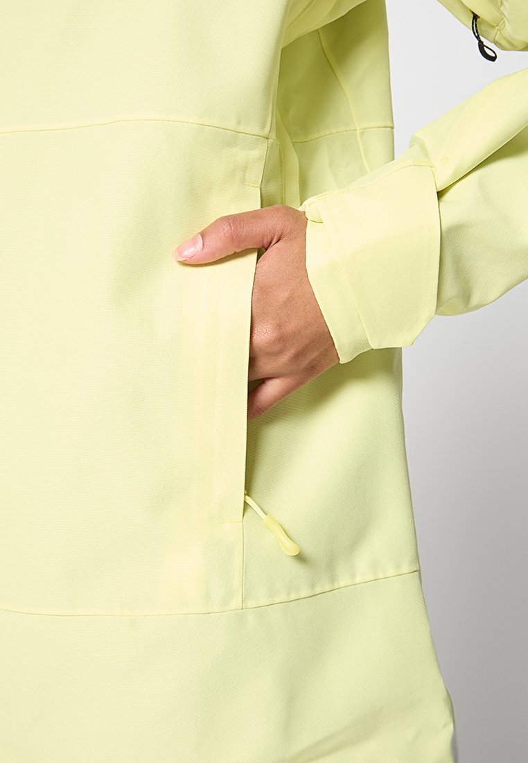 Chaqueta amarillo claro con un acabado texturizado, presenta un bolsillo en ángulo y un detalle de cordón en los puños. Diseño minimalista.