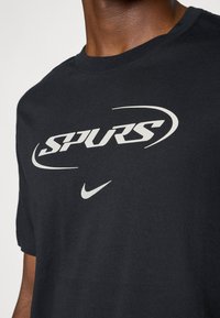 Sort bomulds T-shirt med "SPURS" i fed hvid tekst og et lille hvidt Nike-logo. Korte ærmer og design med rund hals.