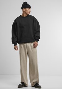 Sweatshirt nero oversize, pantaloni beige a gamba larga e scarpe nere. L'outfit presenta texture morbide e una vestibilità rilassata.