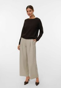 Pullover marrone con collo rotondo abbinato a pantaloni a gamba larga grigio chiaro. Presenta tasche laterali e tacchi squadrati marroni con dettagli.