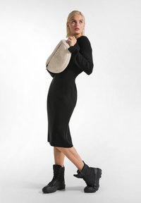 Abito nero lavorato a maglia con maniche lunghe e silhouette aderente, abbinato a una borsa a spalla in pelliccia sintetica color crema e stivali neri stringati.