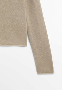 Pull en maille beige au design court, avec un tissu texturé et des manches longues. L'ourlet est légèrement côtelé pour apporter de la structure.