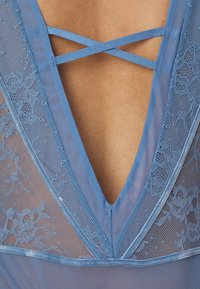 Μπλε δαντελένιο ρούχο με βαθύ σχέδιο V-λαιμόκοψη και διασταυρούμενες τιράντες. Κατασκευασμένο από διάφανο δίχτυ και δαντέλα με λουλούδια και σατέν λεπτομέρειες.