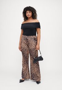 Crna majica bez naramenica, široke hlače s leopard printom u smeđoj i crnoj boji, uparen s malom crnom torbicom i crnim cipelama s oštrim nosom.