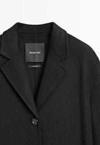 Cappotto di lana nera con rever a punta, chiusura a singolo bottone e una texture morbida. L'etichetta reca la scritta "Massimo Dutti". Design semplice e classico.