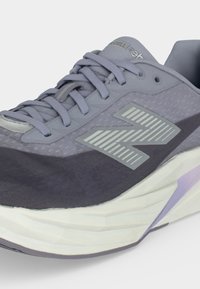 Γκρι και μωβ αθλητικό παπούτσι New Balance με λευκή χοντρή σόλα και κορδόνια, που δείχνει την πλαϊνή όψη και το λογότυπο στο επάνω μεστό υλικό.