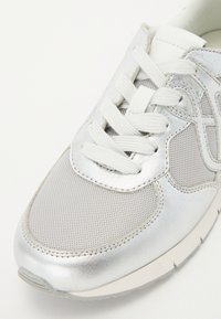 Scarpa da ginnastica argento con parte superiore in rete testurizzata, lacci morbidi e una finitura metallica liscia. Suola in gomma solida per una buona trazione.
