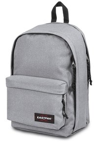 Mochila de tela gris con un bolsillo frontal, cremalleras negras y un asa colgante. Presenta una textura suave y un diseño minimalista.