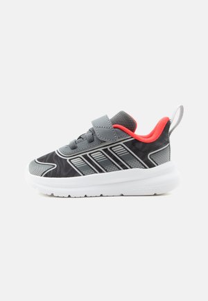 Sneaker per bambini nero e grigio con fodera rossa, suola bianca, strap in velcro e linguetta su sfondo bianco.