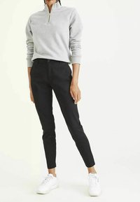 Felpa grigia con zip e polsini a costine, abbinata a pantaloni neri attillati e scarpe da ginnastica bianche. Design semplice e texture morbide.