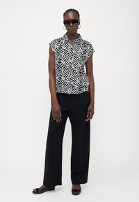 Μαύρο και άσπρο κοντομάνικο πουκάμισο με σχέδιο από φύλλα, συνδυασμένο με φαρδιά μαύρα παντελόνια και μαύρες μπαλαρίνες. Γυαλιά ηλίου και κρίκοι σκουλαρίκια.