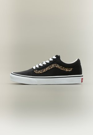 Baskets basses noires avec lacets blancs, semelle blanche et détail de bande latérale imprimée léopard sur un fond clair uni.