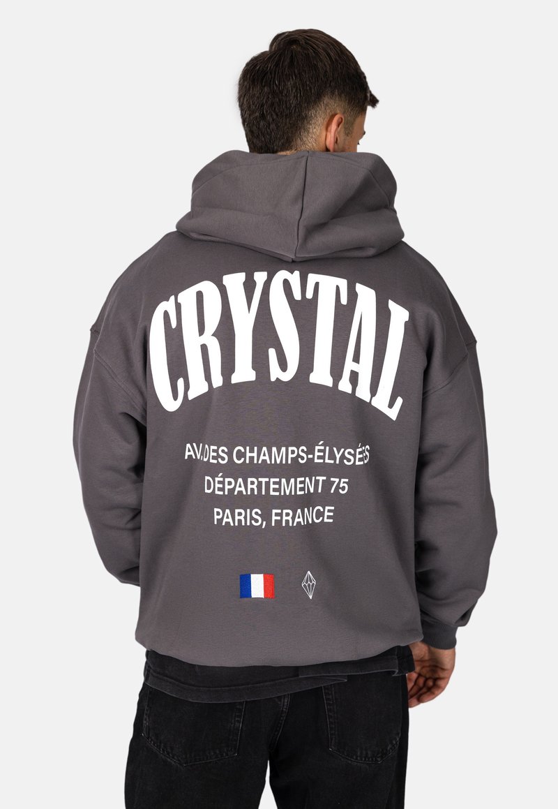 Felpa grigia con grande testo bianco che recita "CRYSTAL" e "AV. DES CHAMPS-ÉLYSÉS", con un dettaglio della bandiera francese e un logo a forma di diamante.