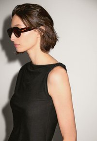 Black sleeveless top with a textured finish, featuring a slight gather at the shoulder. Brown tortoiseshell sunglasses complete the look.