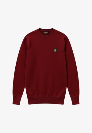 Maglione bordeaux con scollo rotondo, maniche lunghe e piccola toppa rettangolare nera e dorata sul lato sinistro del petto.