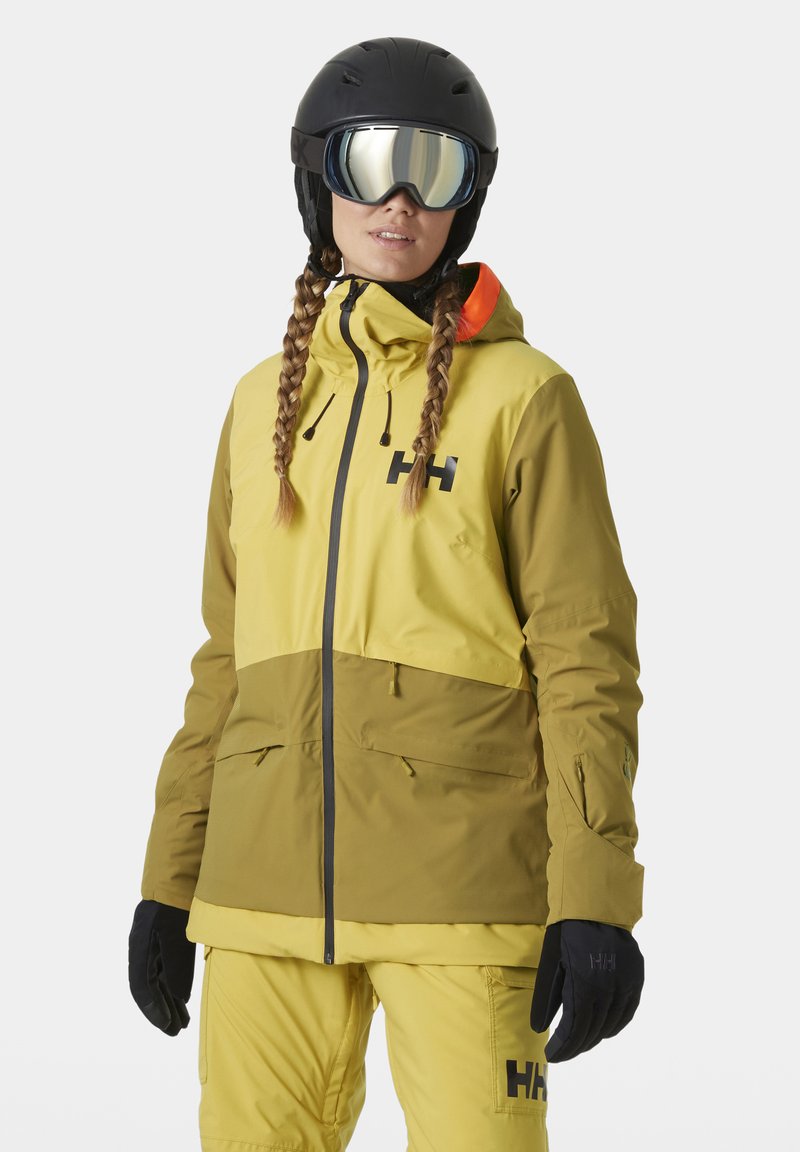 Skijacke mit einem zweifarbigen Design in Gelb und Oliv, aus wasserdichtem Material, mit hohem Kragen und verstellbarer Kapuze.