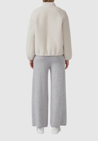 Fleece bomberjack in gebroken wit met een gestructureerde afwerking, gecombineerd met grijze sweatpants met wijdere pijpen en witte sneakers.