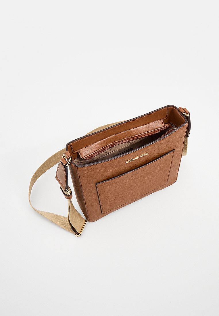 Sac bandoulière synthétique marron avec une fermeture éclair sur le dessus, une poche glissière extérieure, une bandoulière beige réglable et un détail de marque doré sur le devant.