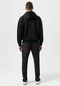 Conjunto atlético negro que incluye una sudadera con capucha y pantalones ajustados, ambos con una textura suave y detalles de malla en las mangas y los lados de los pantalones.