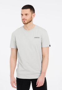 Lichtgrijs t-shirt met korte mouwen en een ronde hals, met een klein zwart "PROTEST" logo op de linkerborst. Glad katoen.