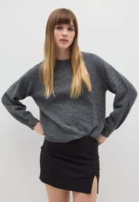 Pull en tricot gris avec des détails scintillants et des manches longues, associé à une mini-jupe noire avec une fente sur le côté.