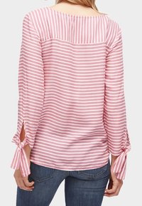 Blusa a righe rosa chiaro con maniche lunghe, caratterizzata da dettagli a fiocco ai polsini e un collo dritto. Realizzata in tessuto morbido e testurizzato.