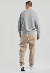 Sweatshirt gris avec un col rond, coupe décontractée ; associé à un pantalon beige ; mannequin portant des baskets blanches ; design simple, sans logos ni motifs visibles.