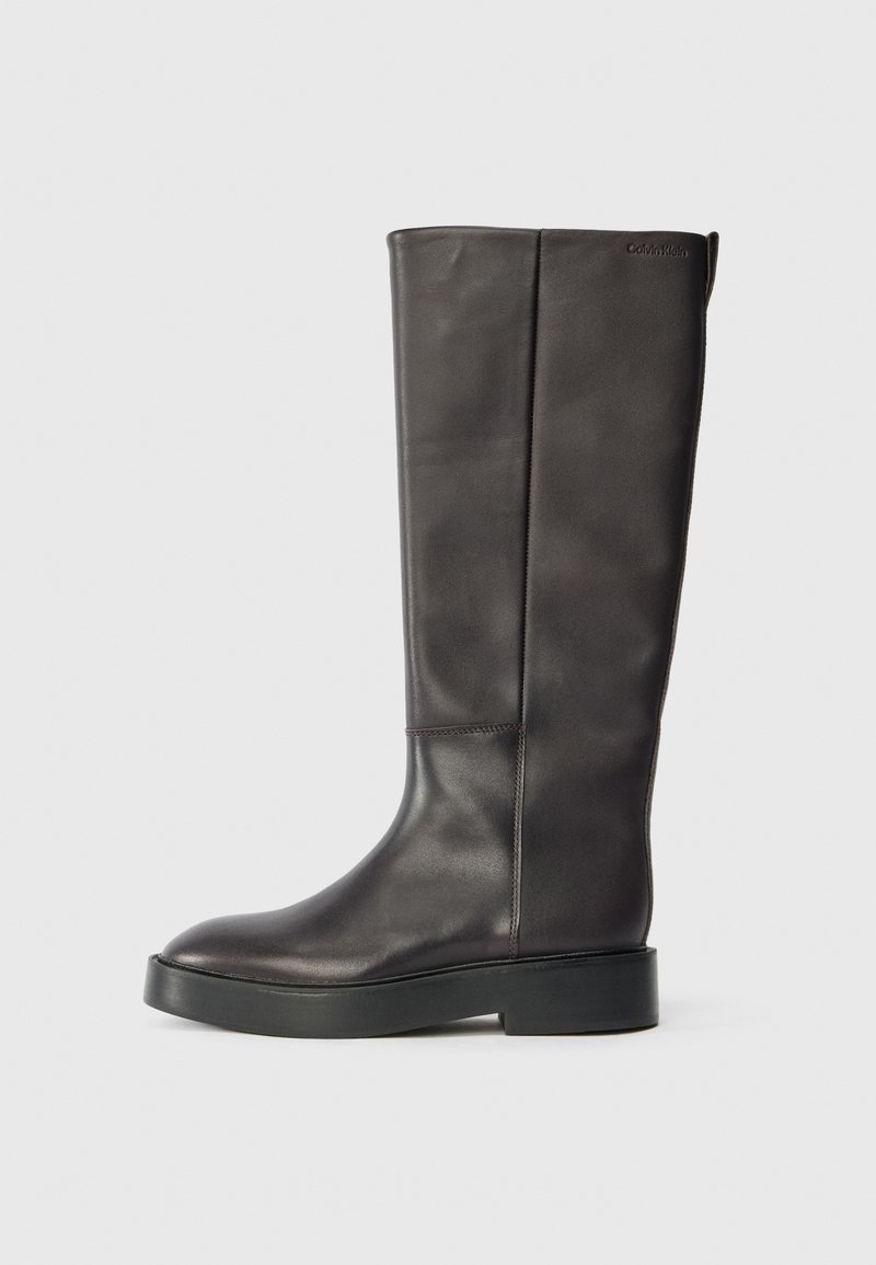 Bota de couro preta até o joelho com sola grossa e logo discreto da Calvin Klein próximo à borda superior, vista de lado.