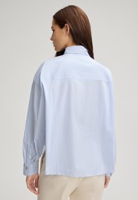 Light blue and white striped long-sleeve shirt with a high collar, buttoned cuffs, and a relaxed fit, showcasing a smooth, soft fabric texture.