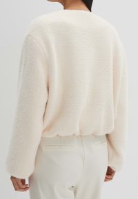 Fluffig, krämfärgad tröja med avslappnad passform, rund halsringning och långa ärmar. Mjuk textur med en något kortare nederkant.