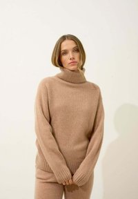 Vaaleanruskea pooloneule, joka on valmistettu pehmeästä neuloksesta; ribbattu kaulus ja hihansuut; rento malli, yhdistettynä samanvärisiin alaosiin.