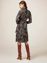 Rochie neagră cu un model, cu guler, mâneci lungi și talie strânsă, cu accente florale aurii. Asortată cu cizme maro până la genunchi.
