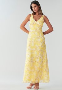 Yellow floral maxi dress with a deep V-neck, fitted bodice, and flowing skirt. Made of lightweight fabric, features a subtle leaf pattern.