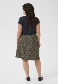 Haut noir à manches courtes associé à une jupe imprimée léopard beige et noire, arrivant au genou. Texture lisse, coupe décontractée, et chaussures plates noires.