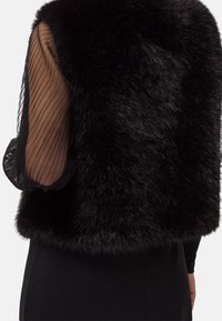 Svart faux fur-väst med en solid blockdesign, som har genomskinliga svarta randiga ärmar och en rundad skärning, vilket ger ett mjukt, texturerat utseende.