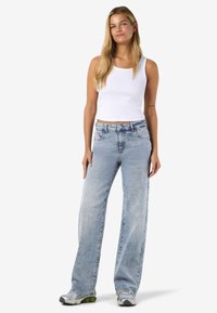 Svetlo praljeni traper hlače širokega kroja z visokim pasom, dopolnjene z belo rebrasto majico brez rokavov in sivimi supergami.