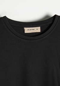 Czarna bawełniana koszulka z okrągłym dekoltem, z wyszywaną krawędzią i metką oznaczoną "diverse", rozmiar M. Gładka struktura bez dodatkowych wzorów.