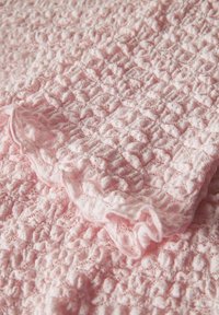 Blødt lyserødt stof med hævet, tekstureret strikkemønster og et afsnit med rynket flæsekant.