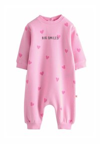 Jumpsuit en coton rose à manches courtes, avec des motifs de cœurs roses et le texte "BIG SMILES" en gris. Dispose de poignets élastiques et d'un col rond.
