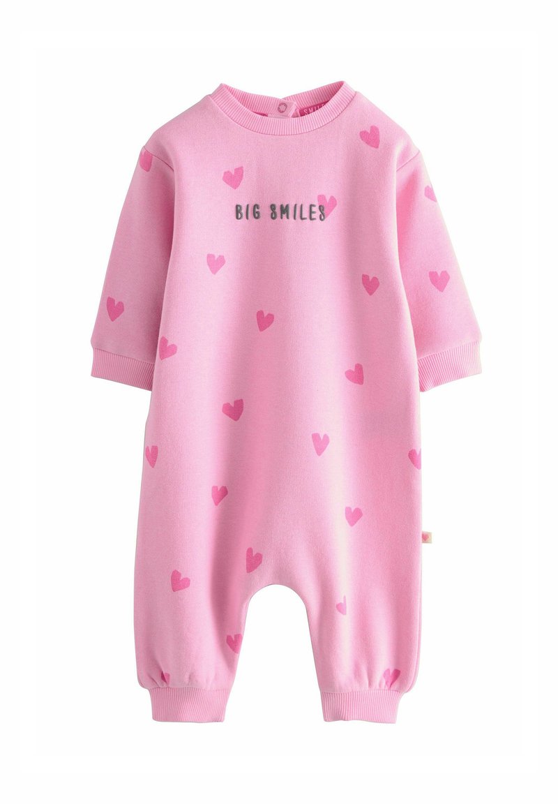Jumpsuit en coton rose à manches courtes, avec des motifs de cœurs roses et le texte "BIG SMILES" en gris. Dispose de poignets élastiques et d'un col rond.