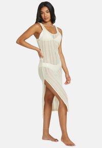 Cremfarbener, gestrickter Maxikleid mit strukturiertem, offenem Gewebe, das seitliche Schlitze und ein tailliertes Oberteil bietet. Ärmelloses Design mit rundem Ausschnitt.
