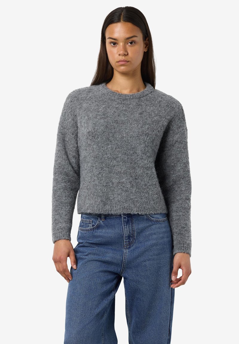 Grauer, flauschiger Strickpullover mit Rundhalsausschnitt und langen Ärmeln. Kürzerer Schnitt, getragen mit blauen Jeans. Weiche Textur, keine sichtbaren Muster.