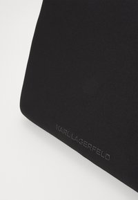 Črna tkanina torbica s gladko teksturo. Značilnosti vtisnjenega logotipa "KARL LAGERFELD" na sprednji strani. Minimalističen dizajn, pravokotna oblika.