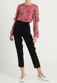 Blusa floral rosa con mangas acampanadas, combinada con pantalones negros ajustados y mules blancos de tacón. Tejido suave, silueta moderna.