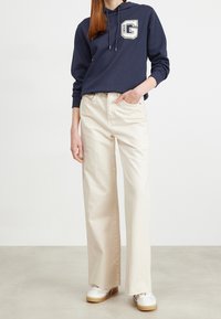 Felpa navy con logo, pantaloni cream a gamba larga e sneakers bianche con suole beige. Tessuto dalla texture morbida e vestibilità comoda.