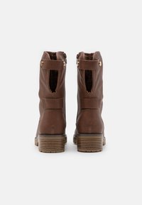 Bottes de cheville en cuir marron avec une surface texturée, fermeture éclair, design loose et talon rayé. Comprend deux accents en métal doré.