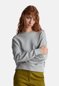 Felpa grigia chiaro con colletto tondo, polsini e orlo a costine. Abbinata a pantaloni verde oliva. Tessuto morbido con vestibilità comoda.