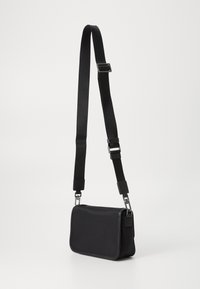 Sacola cruzada preta com formato retangular, feita de tecido suave, apresentando uma alça destacável e detalhes em metal prateado.