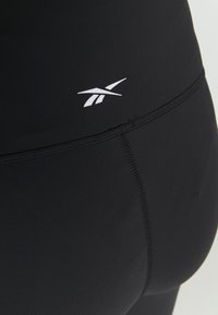 Leggings atléticos pretos com uma textura suave, costuras reforçadas e um pequeno logotipo branco perto da cintura.